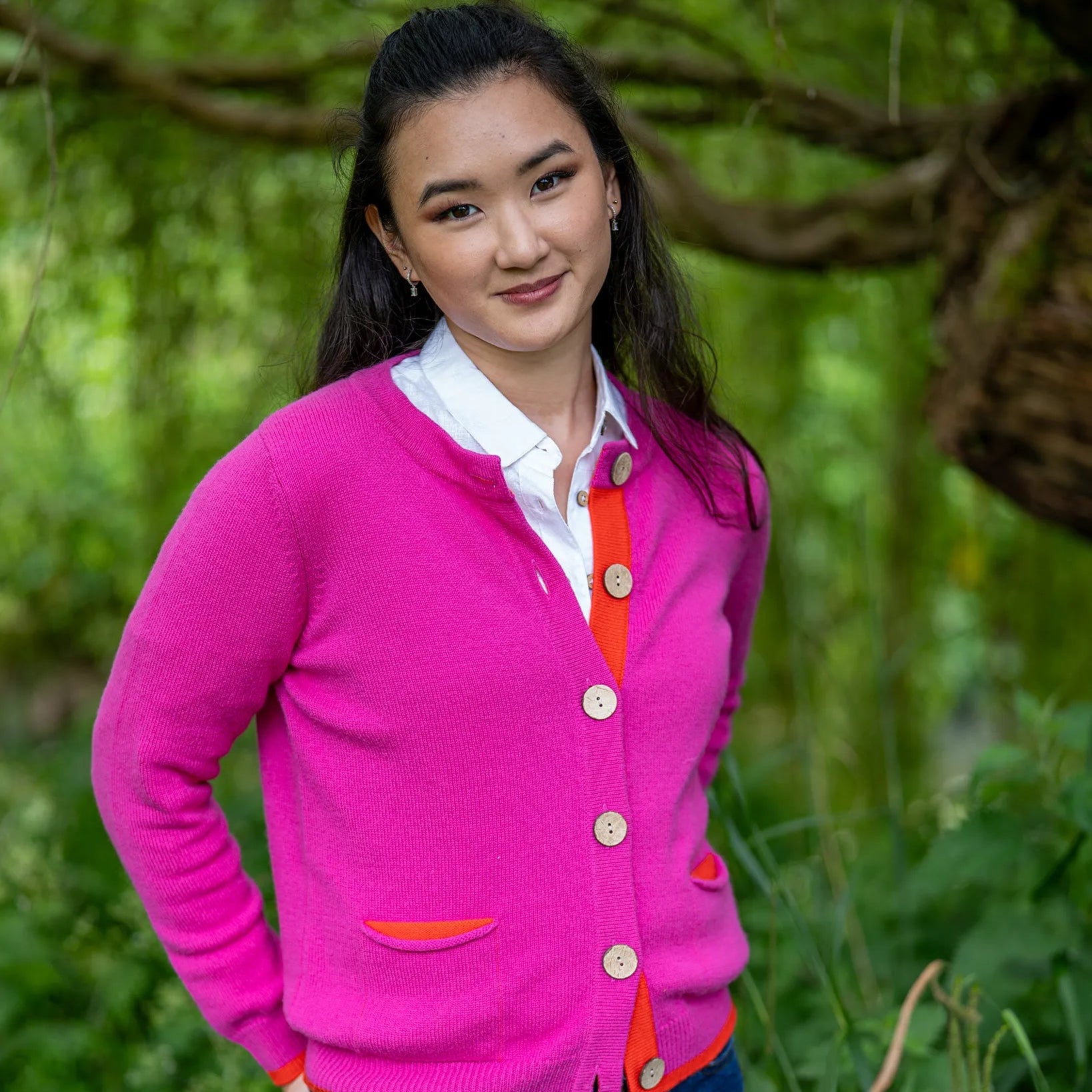 Woman wearing a bright pink cardigan with orange trim in a natural setting