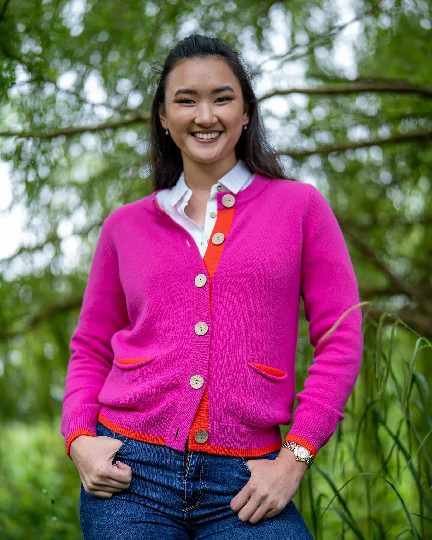 Woman wearing a bright pink cashmere cardigan with orange accents outdoors