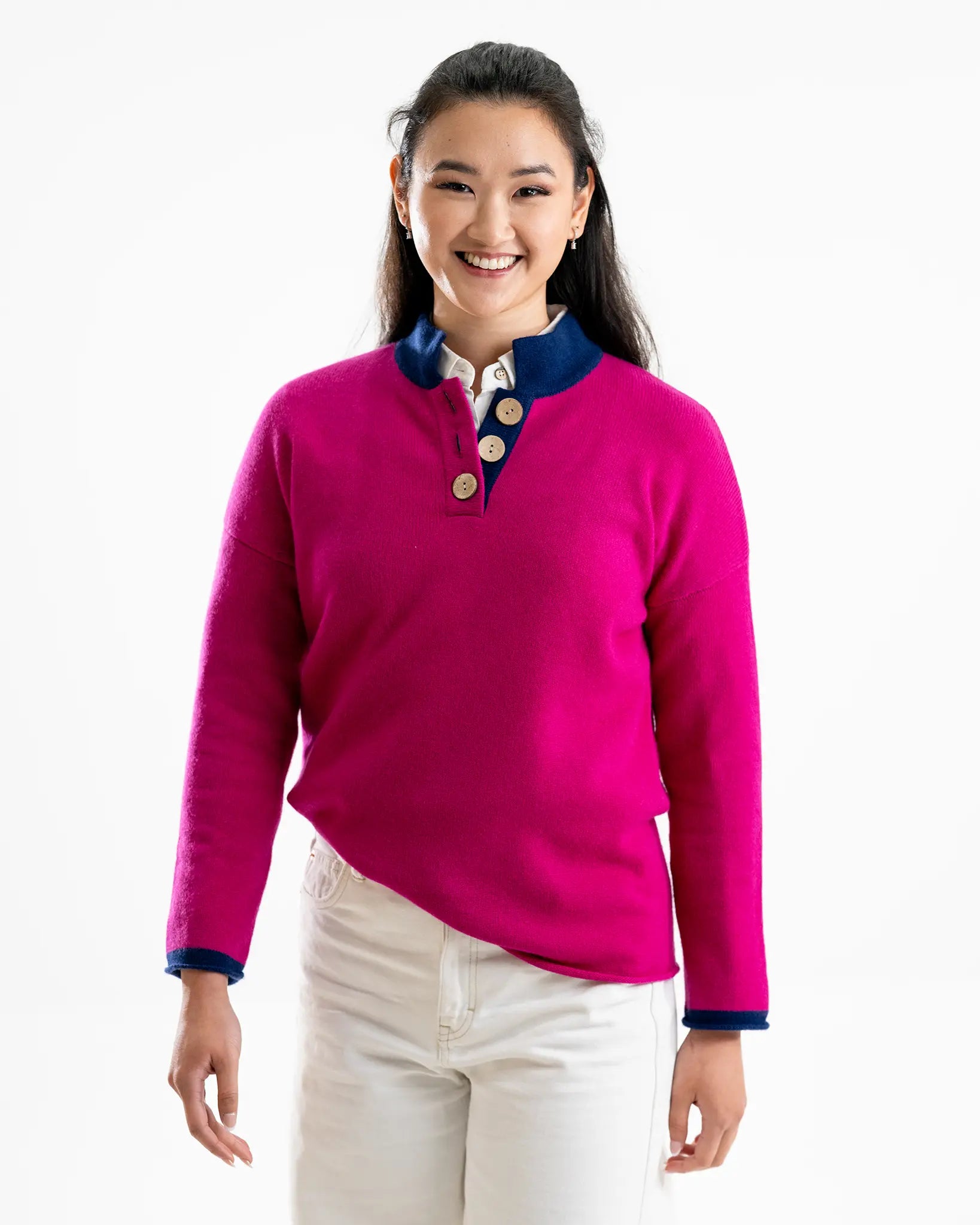 Woman wearing a bright cashmere pink sweater with blue trim on a white background