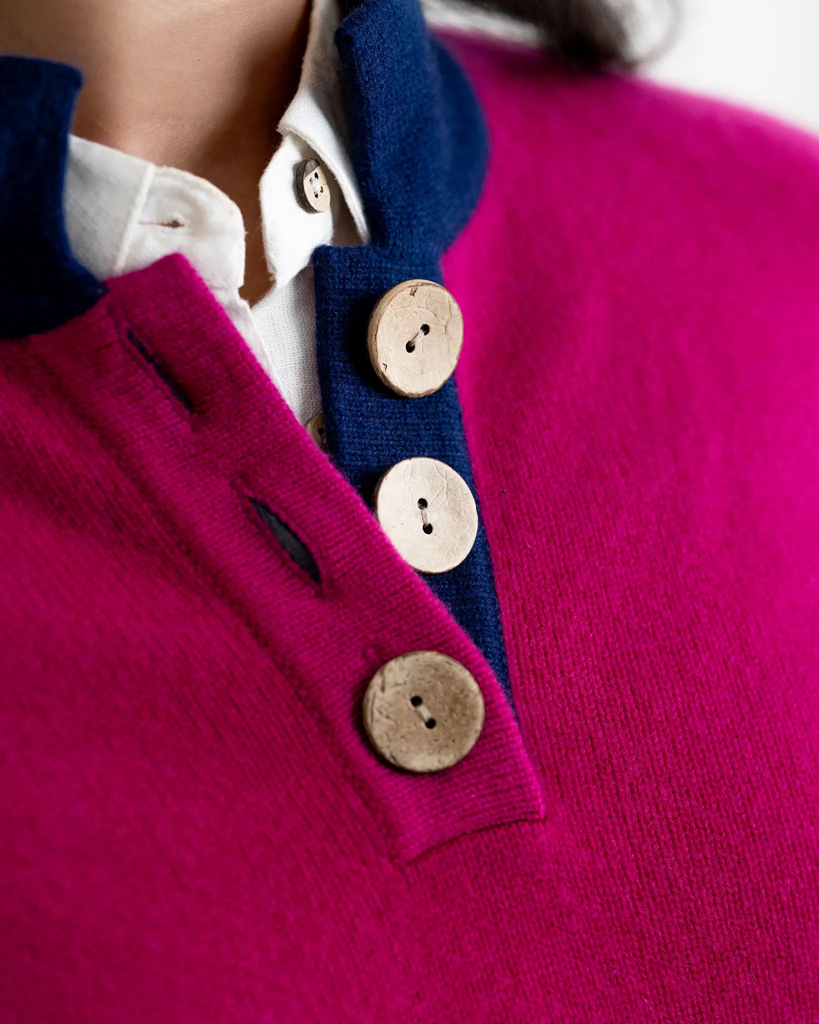 Close-up of a pink sweater with blue collar and coconut buttons.