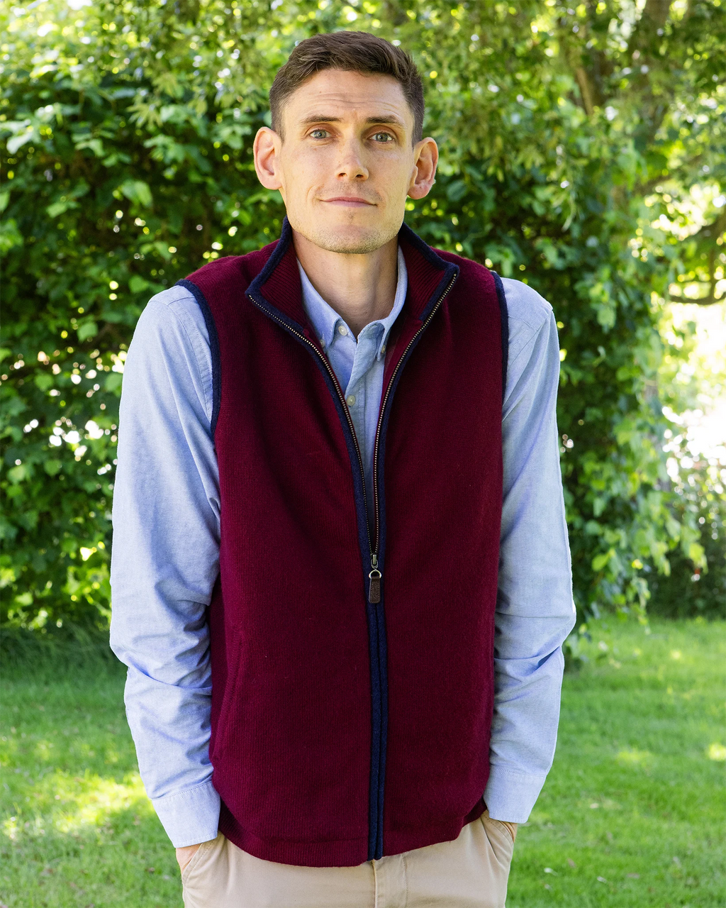 Man wearing a cashmere burgundy gilet lined over a light blue shirt in a country garden setting