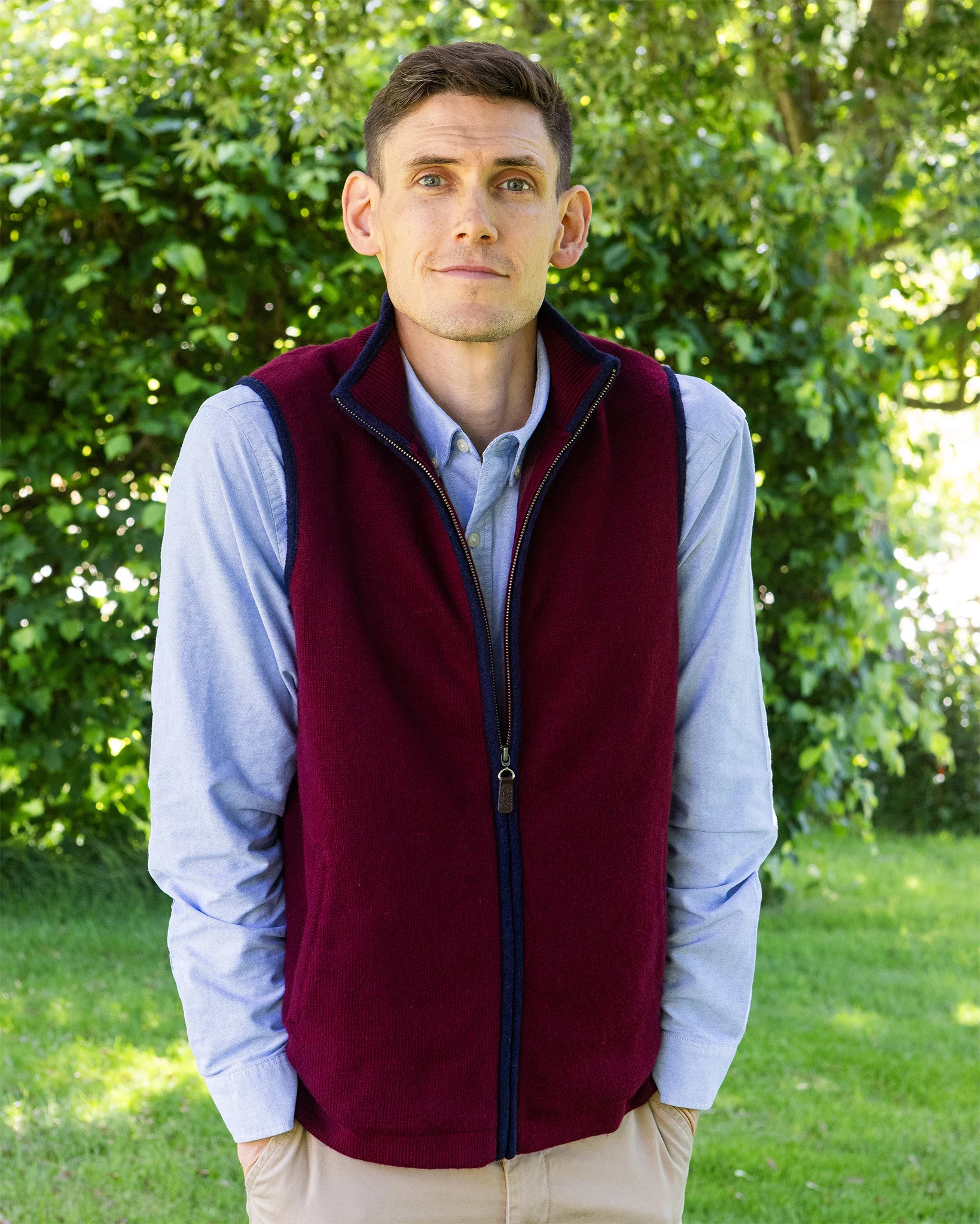 Man wearing a cashmere burgundy gilet lined over a light blue shirt in a country garden setting