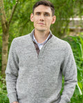 Man wearing a grey sweater in cashmere and merino marl and brown corozo buttons standing in a garden