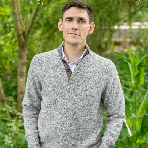 Man wearing a grey sweater in cashmere and merino marl and brown corozo buttons standing in a garden