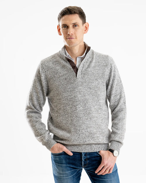 Man wearing a cashmere grey marl sweater with brown corozo buttons with blue jeans on a white background