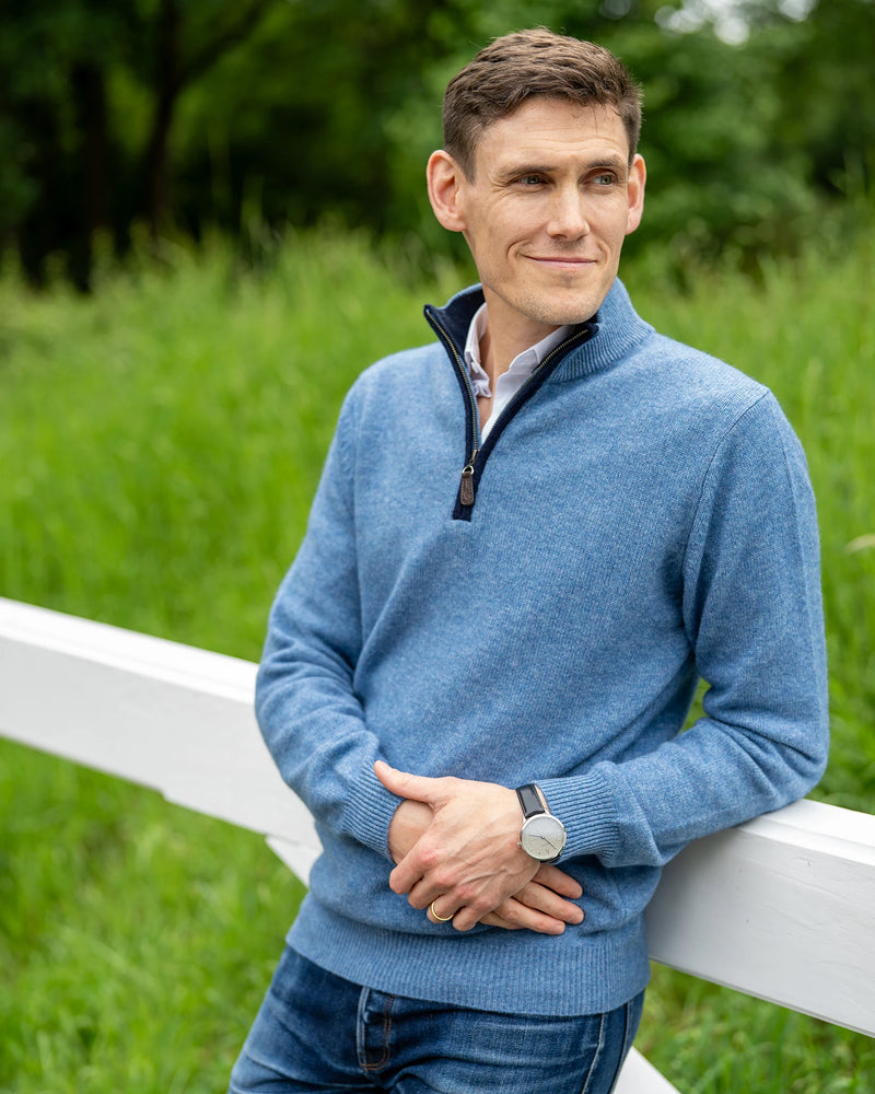 Model leaning against a gate in cashmere and merino sweater in marine blue