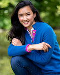 Model wearing high collar jumper in Aztec blue with pink collar and cuffs and large coconut buttons by river setting