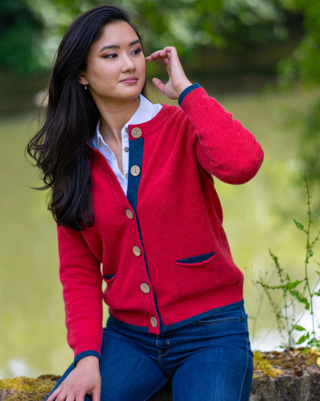 Women on wall wearing orange red cardigan with navy pockets and trim in countryside