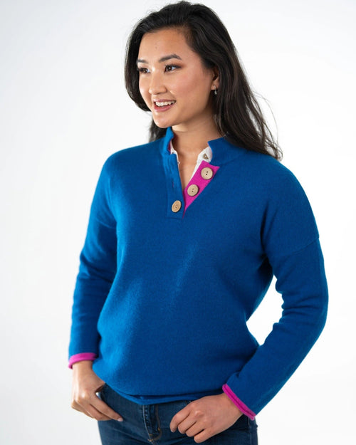 Women wearing high collar jumper sweater in blue with cerise cuffs and neck and large coconut buttons
