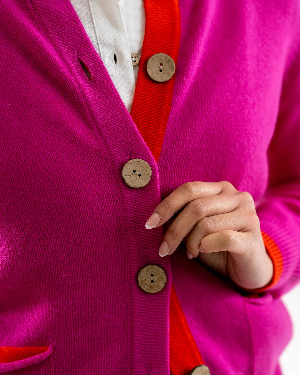 Close-up of a bright pink cardigan with orange trim and coconut buttons