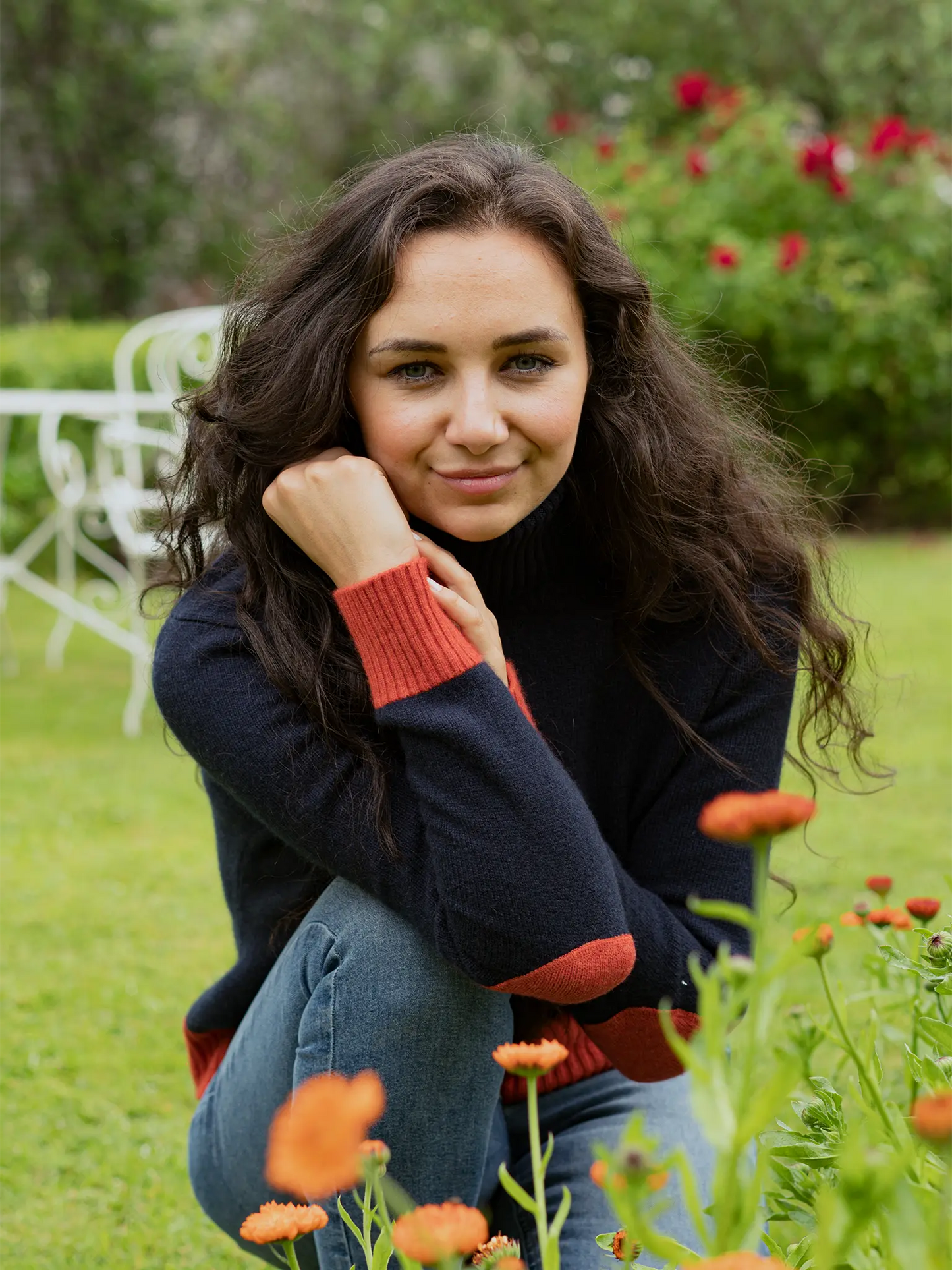 model wearing roll neck navy jumper with burnt orange cuff ends elbow patches and hem in garden with flowers